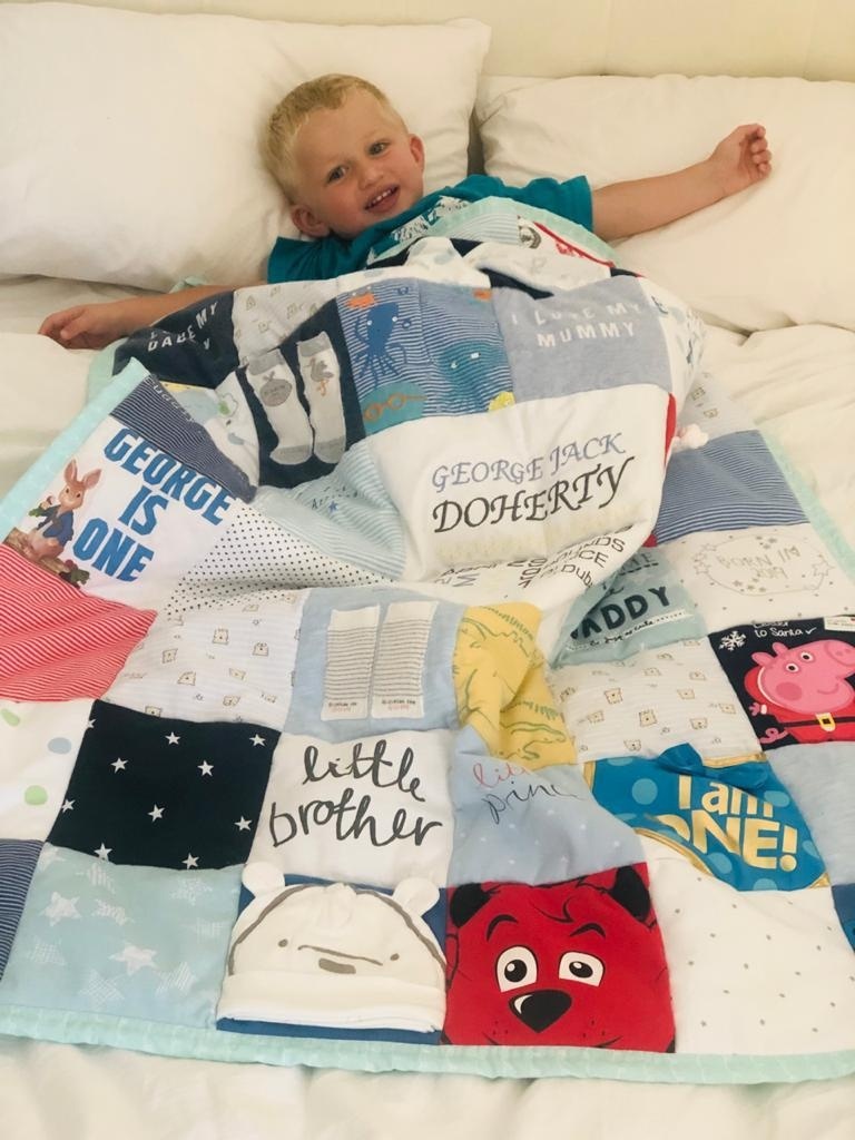 A little girl smiling on a bed with a handmade pink memory quilt
